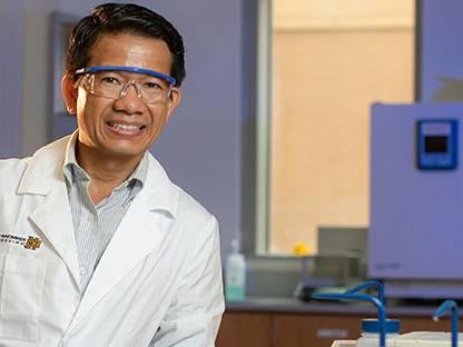 Man with safety goggles and lab coat smiling for a picture